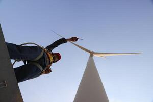 Specialist wind turbine technician working at the base of the turbine. Wind turbine service technician wearing safety uniform and safety harness working at windmill farm photo