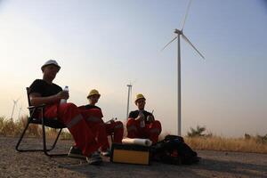 retrato molino ingeniero equipo con rojo trabajo uniforme con la seguridad difícil sombrero y aprovechar trabajo en viento turbina granja foto