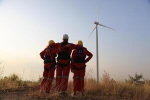 Portrait Windmill engineer team with red work uniform with safety hard hat and harness work in wind turbine farm photo