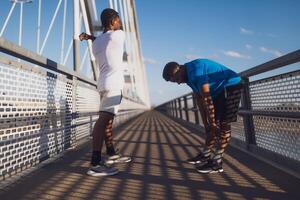 Two african-american friends are exercising on the bridge in the city. They are warming up for jogging. photo