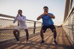 Two african-american friends are exercising on the bridge in the city. They are doing squats. photo