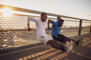 Two african-american friends are exercising on the bridge in the city. They are doing reverse push-ups. photo