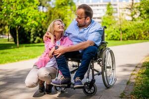 Man in wheelchair is spending time with his friend in park. photo