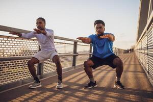 Two african-american friends are exercising on the bridge in the city. They are doing squats. photo