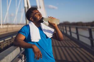 Portrait of young african-american man who is drinking water and relaxing after jogging. photo
