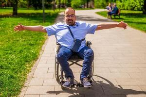 retrato de contento hombre en silla de ruedas. él es disfrutando soleado día en ciudad parque. foto