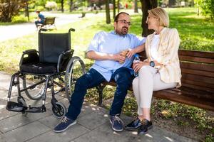 Man in wheelchair is spending time with his mother in park. photo