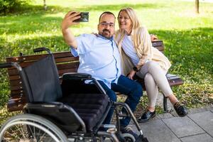 hombre en silla de ruedas es gasto hora con su madre en parque. ellos son tomando autofoto foto