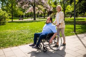 Man in wheelchair is spending time with his mother in park. They are enjoying sunny day together. photo