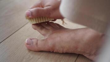 Using a brush, the person gently brushes their foot on the hardwood flooring video