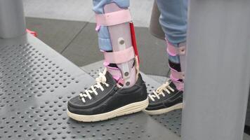 un' poco ragazza nel ortesi scarpe croci un' di legno ponte bambino cerebrale paralisi disabilità. video