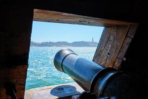 View out of a gunport in hull of the ship on the gun deck over the gun cannon muzzle in photo