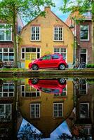 Red car on canal embankment in street of Delft. Delft, Netherlands photo