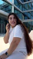 Happy young woman sitting on the bench on the public area, typing chat message on smartphone, smiling girl use cell phone chatting, searching information on browser wireless internet, online shopping video