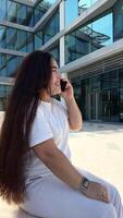 Happy young woman sitting on the bench on the public area, typing chat message on smartphone, smiling girl use cell phone chatting, searching information on browser wireless internet, online shopping video