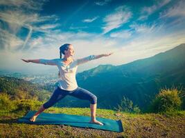 Woman doing yoga asana Virabhadrasana 2 Warrior pose outdoors photo