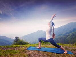 Woman doing yoga asana Virabhadrasana 1 - Warrior pose outdoors photo