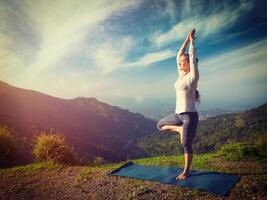 Woman in yoga asana Vrikshasana tree pose in mountains outdoors photo