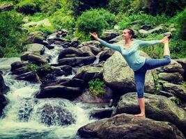 Woman doing yoga asana Natarajasana outdoors at waterfall photo