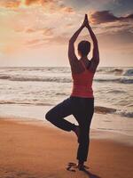 Young sporty fit woman doing yoga tree asana on beach photo