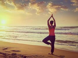 Young sporty fit woman doing yoga tree asana on beach photo