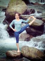 Woman doing Ashtanga Vinyasa Yoga asana outdoors at waterfall photo