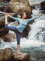 Woman doing yoga asana Natarajasana outdoors at waterfall photo