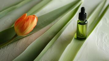 A bottle of green oil is placed on the long leaves, with an orange tulip next to it. photo