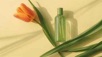 A bottle of green oil is placed on the long leaves, with an orange tulip next to it. photo