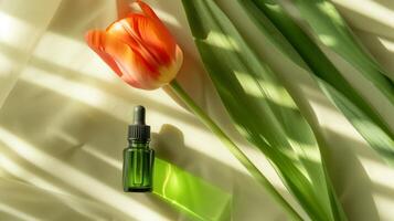 A bottle of green oil is placed on the long leaves, with an orange tulip next to it. photo