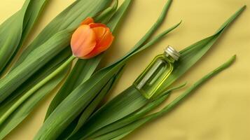 A bottle of green oil is placed on the long leaves, with an orange tulip next to it. photo