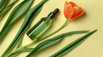 A bottle of green oil is placed on the long leaves, with an orange tulip next to it. photo