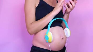 pregnant woman putting music with headphones on her tummy, pink background video