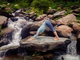 Young sporty fit woman doing yoga oudoors at tropical waterfall photo