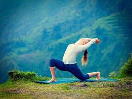 Sporty fit woman practices yoga asana Anjaneyasana in mountains photo