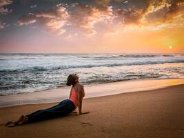 Woman practices yoga asana Urdhva Mukha Svanasana at the beach photo