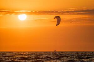 Kiteboarding kitesurfing kiteboarder kitesurfer kites silhouette in the ocean on sunset photo