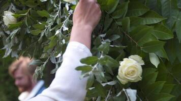 bloemisten monteren, versieren met bloemen boog voor bruiloft ceremonie. binnenhuisarchitecten werken Bij evenement, verjaardag, verjaardag, feest. evenement decoratie met vers bloemen. rustiek stijl. ontwerper Bij werk. video