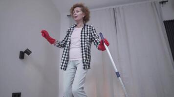 Senior woman is cleaning up before moving into a new apartment dancing and singing along to my floor with a mop. Excited woman enjoying housekeeping. People, housework and housekeeping concept. video