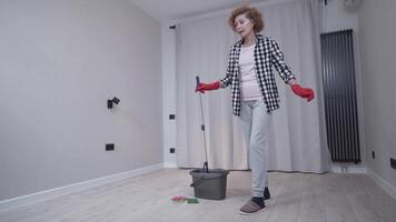 Cheerful mature female cleaning a new apartment without furniture, mopping the floor with a mop dances and sings. Be creative about cleaning your home. People, housework and housekeeping concept. video