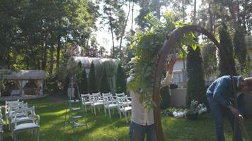 Floristen montieren, schmücken mit Blumen Bogen zum Hochzeit Zeremonie. Dekorateure Arbeiten beim Fall, Geburtstag, Jubiläum, Party. Veranstaltung Dekoration mit frisch Blumen. rustikal Stil. Designer beim arbeiten. video