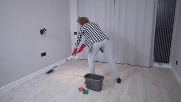 People, housework and housekeeping concept. Senior woman mopping floor. A mature female washes the floor in a new apartment without furniture. Cleaning before moving to new apartments video