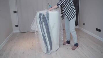 Mature woman unpacking new bed mattress while moving into new apartment. Happy elderly woman unpacking new orthopedic mattress in an empty living room. Furnishing new house. Renting a house. video