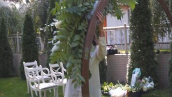 profissional florista trabalhador decora festivo arco para cerimonial casamento cadastro. mulher instalando Casamento decoração. decorador decorar arco ao ar livre Casamento cerimônia com flores e vegetação. video