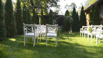 Wedding decor for outdoor cerimony. Wedding arch and chairs for guests in white color on green grass in sunny weather. Backyard wedding venue. Furniture and decoration for outside wedding party. video