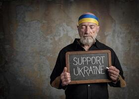 support Ukraine words on a blackboard held by senior man photo