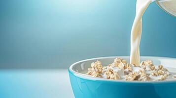 Pouring fresh milk into bowl of cereal on blue background on a sunny morning for breakfast photo