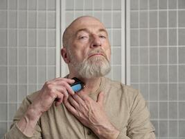 senior man is grooming his beard with electric razor photo