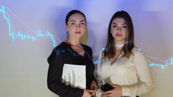 Two confident professional business woman in the office against the background of cryptocurrency chart video