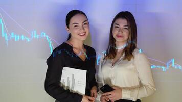 Two confident professional business woman in the office against the background of financial chart video